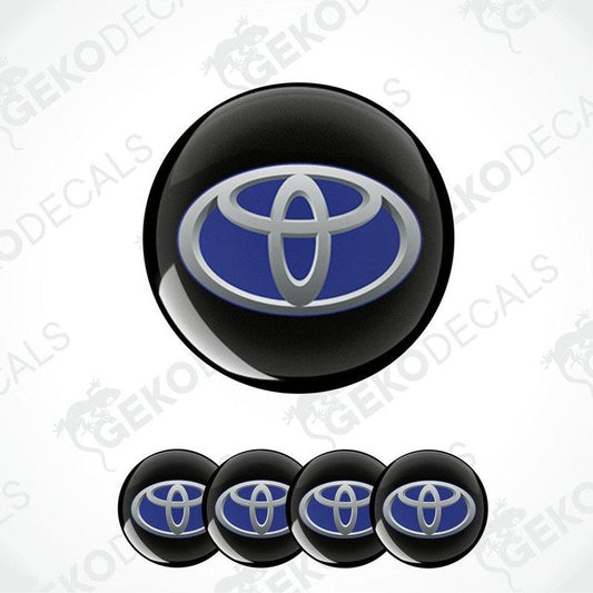 A set of four vinyl stickers with a Toyota brand logo, including two in black with a blue and silver Toyota emblem, and two in gray with a blue and silver Toyota emblem.