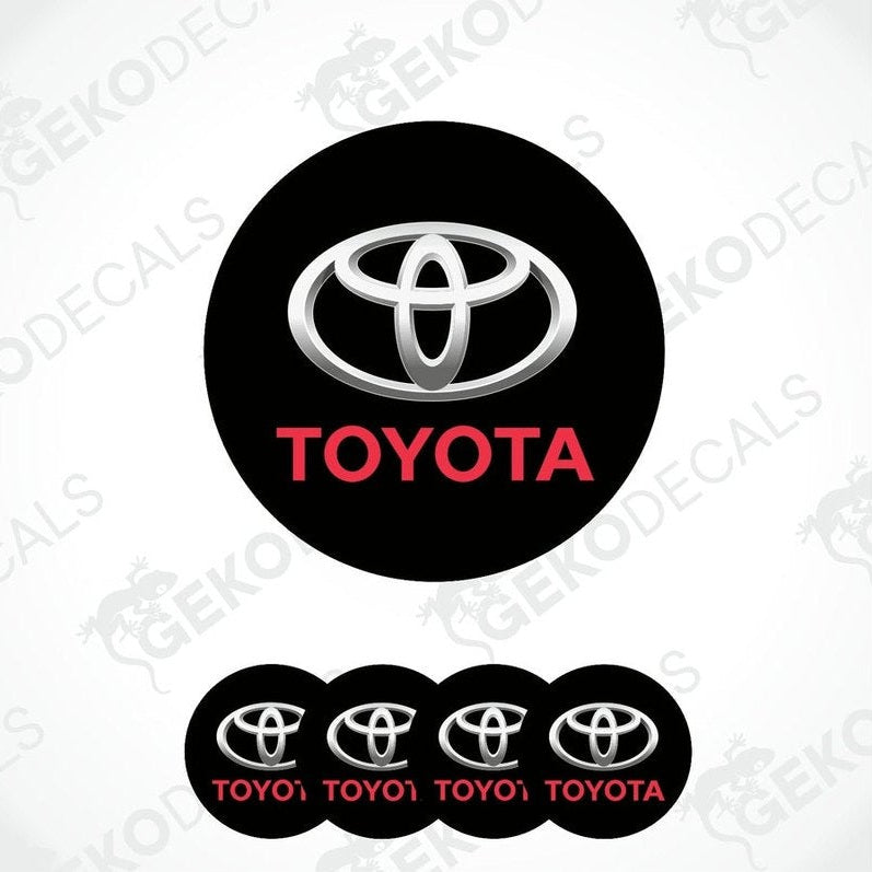 A set of black, white, and red Toyota wheel decals. The main decal is circular with the Toyota logo in white and red on a black background.