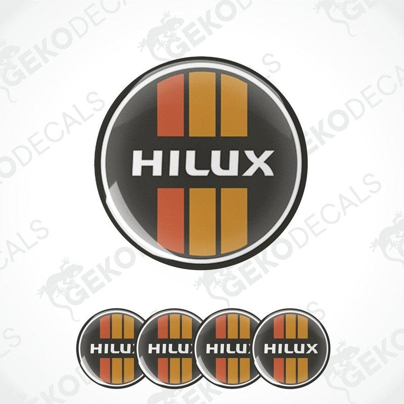 A set of four red, orange, and black vinyl stickers with the word 'HILUX' on them, arranged in a circular pattern with a white background.